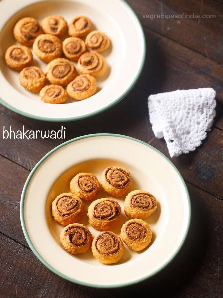 bhakarwadi pinwheels served in a green rimmed ceramic bowl with text layovers.