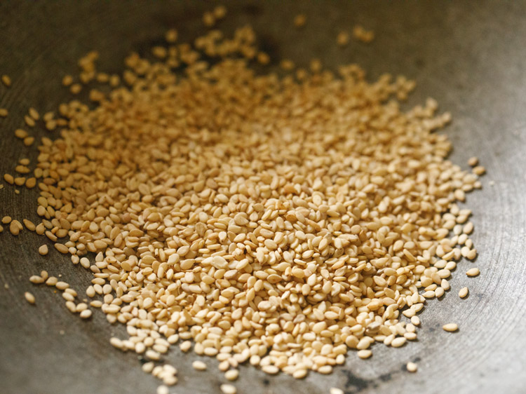 white sesame seeds added to hot heavy pan for making stuffing for bhakarwadi recipe. 