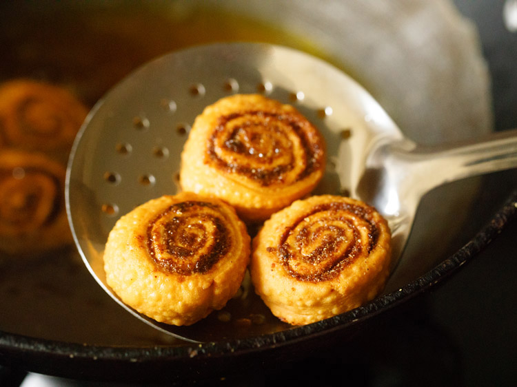 removing fried bakarwadi with a slotted spoon. 