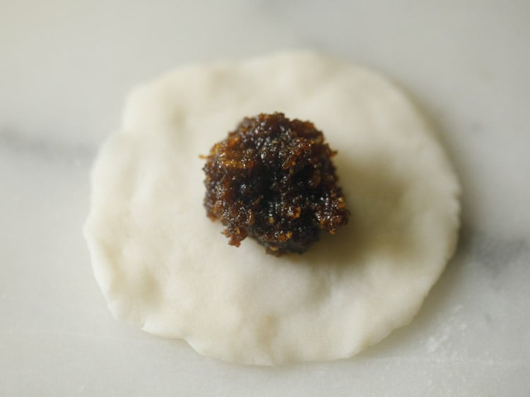 prepared coconut-jaggery stuffing placed in the center of the flattened dough. 