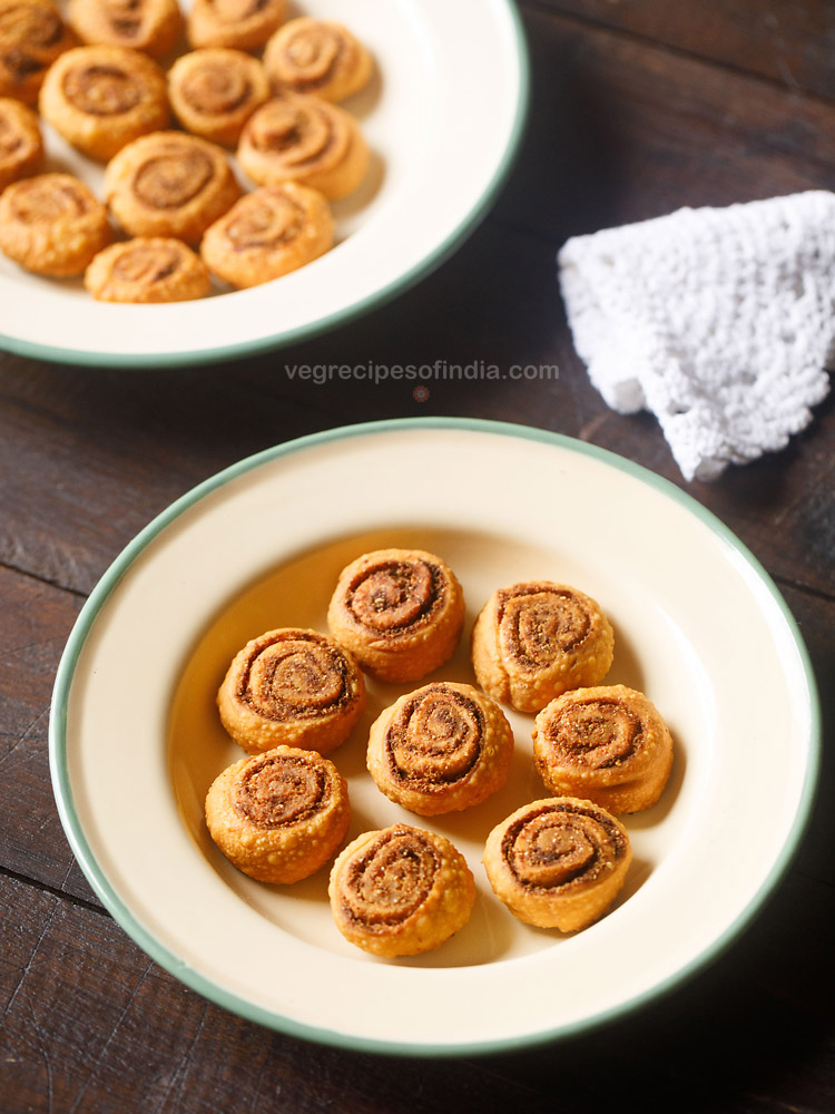 bhakarwadi pinwheels served in a green rimmed ceramic bowl with text layover. 