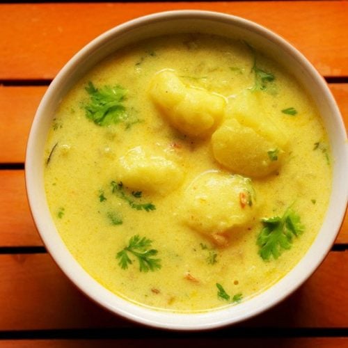 closeup shot of dahi aloo in a bowl on an orange wooden board.