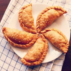 gujiya arranged neatly on a white plate placed on a white and blue checkered napkin