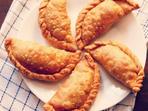 gujiya arranged neatly on a white plate placed on a white and blue checkered napkin.