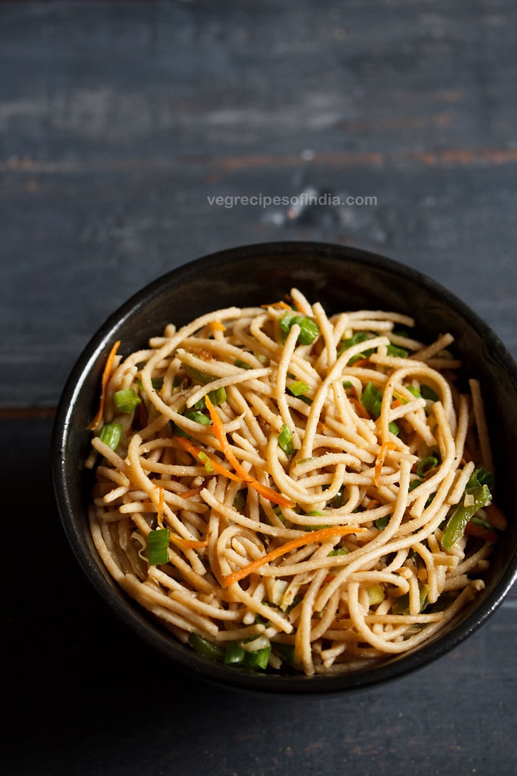 veg noodles served in a black bowl on a dark blue-gray wooden board