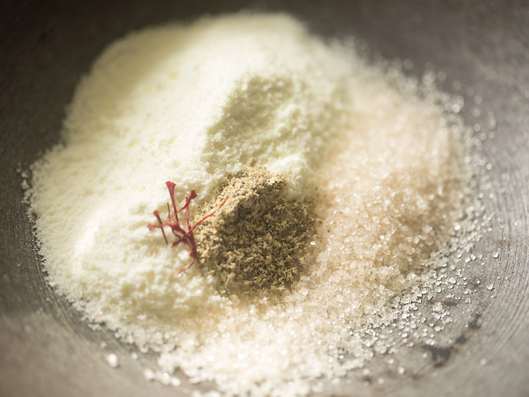 milk powder, sugar, saffron strands and cardamom powder added to a heavy pan for making stuffing for chom chom. 