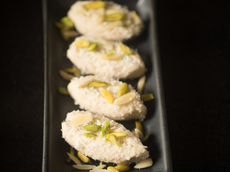 cham cham pieces garnished with sliced pistachios and almonds and placed on a black platter. 