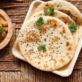 kulcha garnished with coriander leaves and served on a wooden plate.