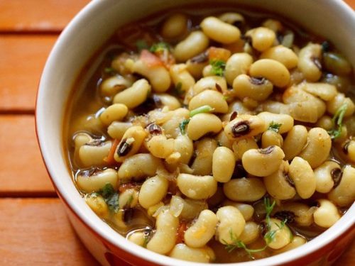 overhead shot of lobia masala in a ceramic bowl on an orange tray.