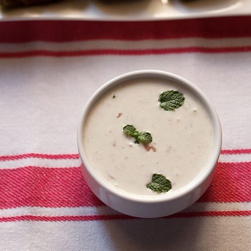 onion raita in a white bowl on a pink and white linen