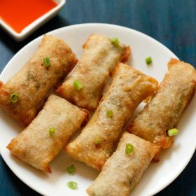 white serving plate with 6 crispy fried veggie spring rolls garnished with green onions