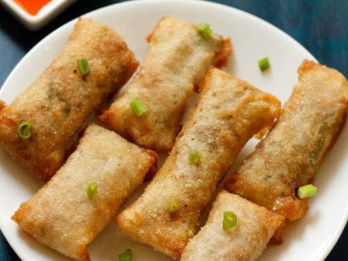 white serving plate with 6 crispy fried veggie spring rolls garnished with green onions