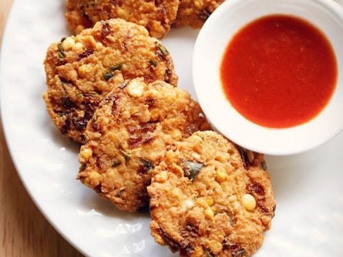dal vada arranged neatly on a white plate next to a small white bowl of red chutney.