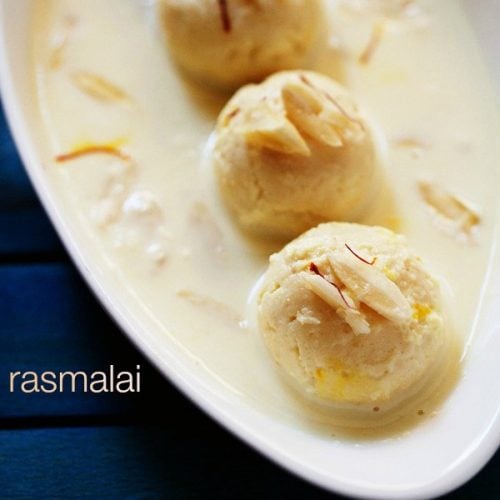 4 balls of rasmalai in an oblong white serving dish covered with thickened milk and garnished with sliced almonds and saffron threads