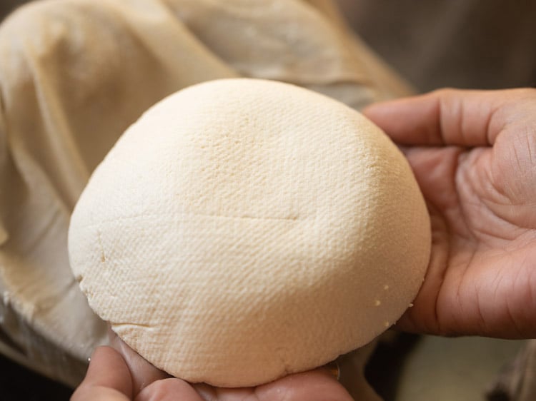 a round block of homemade paneer held with fingers