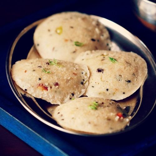 Top shot of four round oats idli arranged on silver plate on a dark blue wooden tray