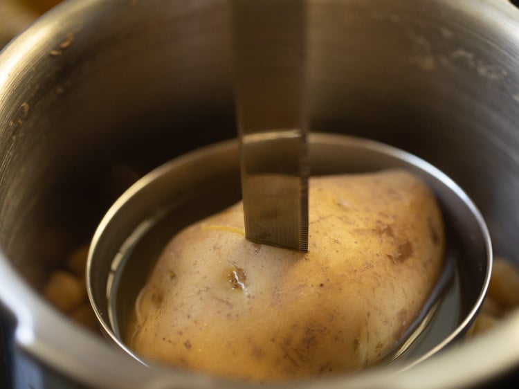 sliding a fork or knife in the cooked potato to check if it is cooked or not