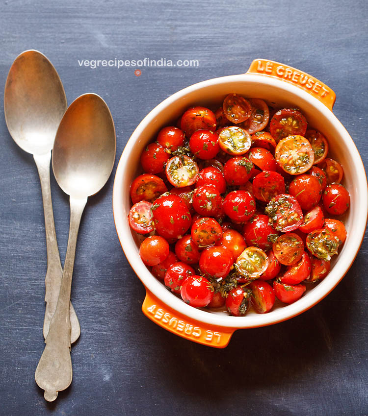 ensalada de tomate cherry servida en un bol con dos cucharas a un lado. 