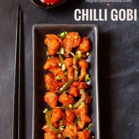 chilli gobi served in a black rectangular tray with black chopsticks on the left side on a blacking grey board with sweet red chilli sauce in a small black bowl placed on top.