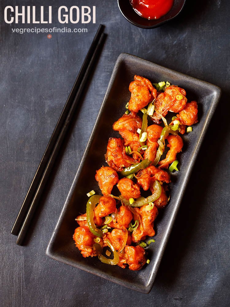 chilli gobi served in a black rectangular tray with black chopsticks on the left side on a blacking grey board