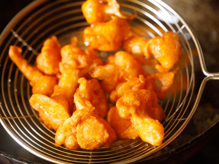 removing fried cauliflower florets with a spider spoon