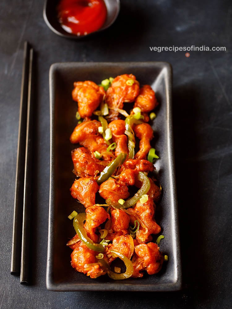 chilli gobi served in a black rectangular tray with black chopsticks on the left side on a blacking grey board