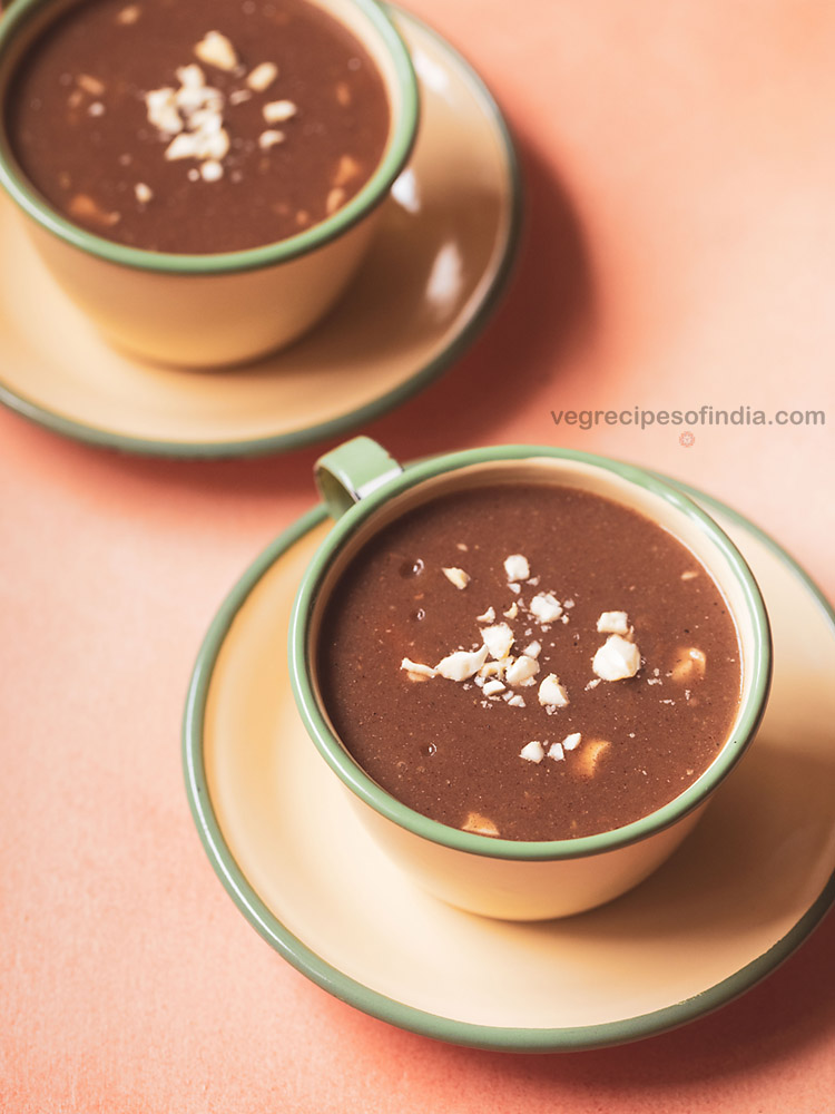 ragi malt garnished with some chopped cashews and served in two cups 