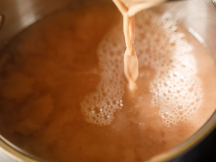 pouring ragi slurry in the hot water contained in the saucepan