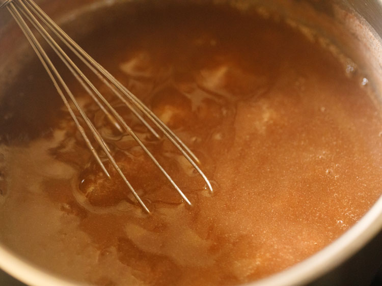 mixing jaggery in the cooked ragi mixture with a wired whisk. 