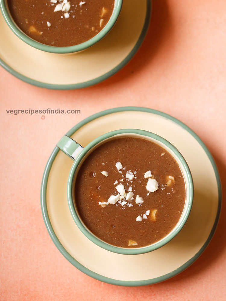 ragi porridge garnished with some chopped cashews and served in a cream colored cup with saucer. 