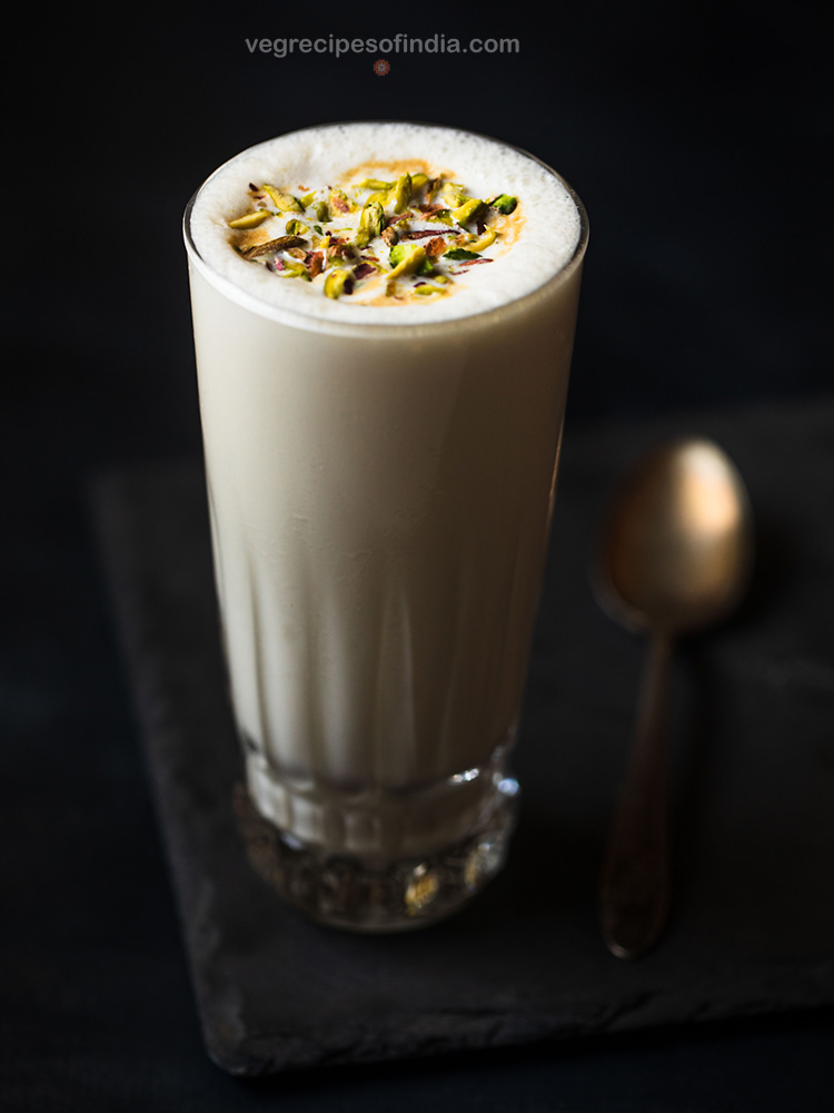 vanilla milkshake served in a tall glass kept on a dark grey slate board which is kept on top of a black board