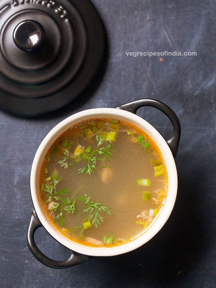 lemon coriander soup served in a black bowl with handles with a soup spoon on the side on a dark bluish grey background.