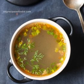 lemon coriander soup served in a black bowl with handles with a soup spoon on the side on a dark bluish grey background with text layovers.