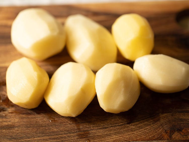 rinsed and peeled potatoes on a wooden surface.