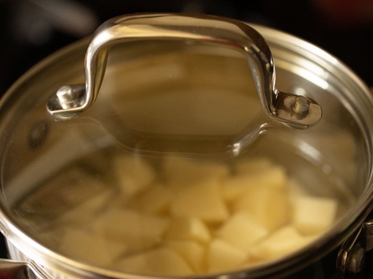 pan covered with a glass lid and kept on stove top for cooking potatoes