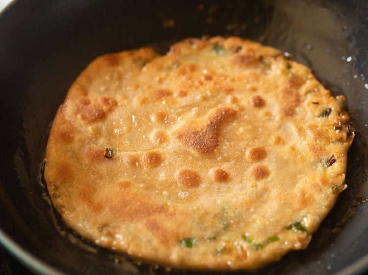 scallion pancake flipped again, with golden blisters showing on top.