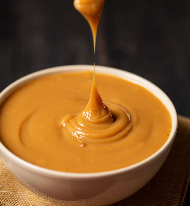 dulce de leche in a white bowl with a spoon pulling some out of the bowl.