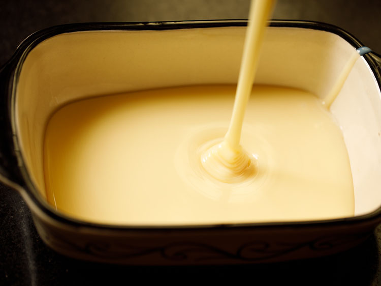 pouring sweetened condensed milk into an enamel loaf pan.