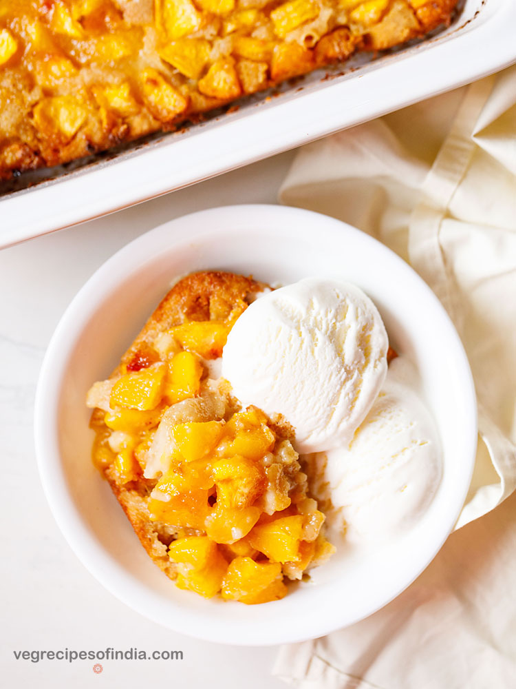 homemade peach cobbler in a bowl with two scoops of vanilla ice cream.