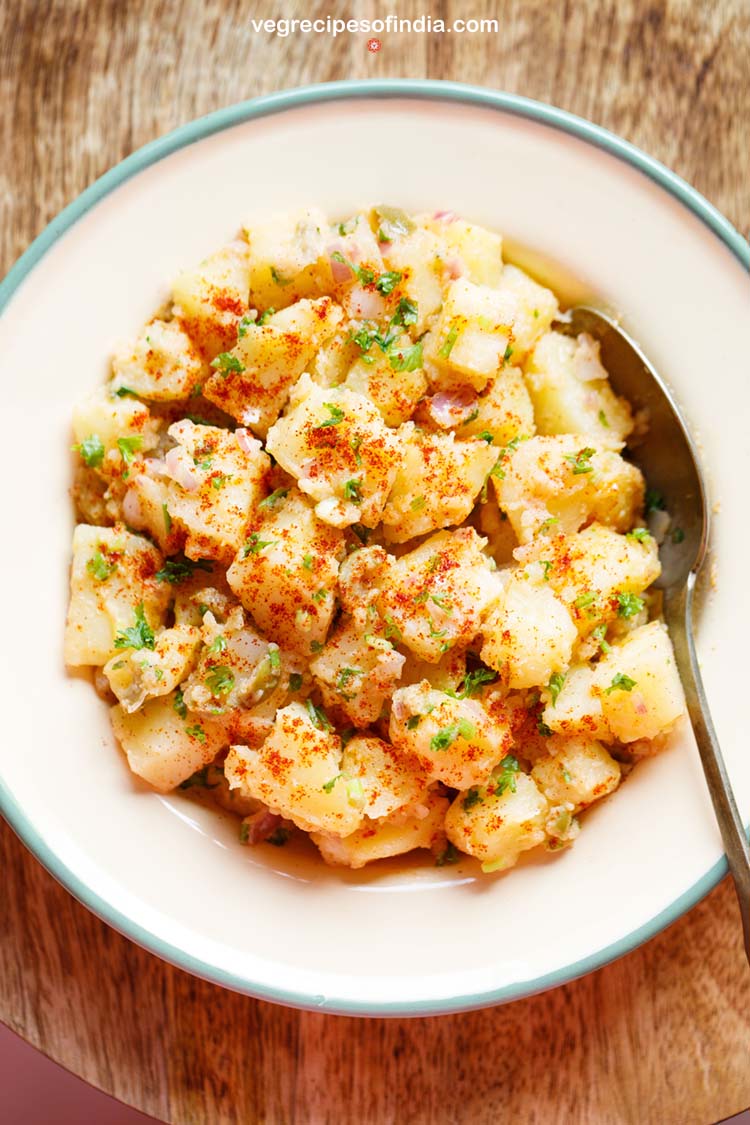 potato salad with a spoon at side, garnished with parsley, specks of paprika served in a cream enamel plate.