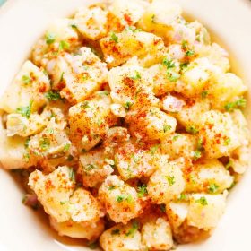 potato salad garnishesd with parsley, specks of paprika served in a cream enamel plate