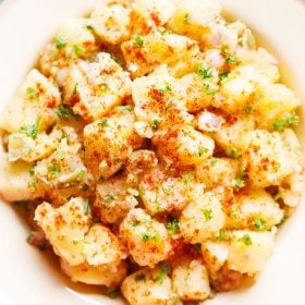 potato salad topped with parsley, specks of paprika served in a cream enamel plate