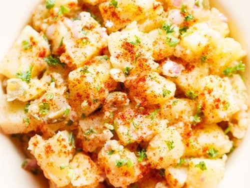 potato salad topped with parsley, specks of paprika served in a cream enamel plate