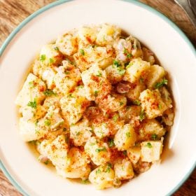 potato salad topped with parsley, specks of paprika served in a cream enamel plate