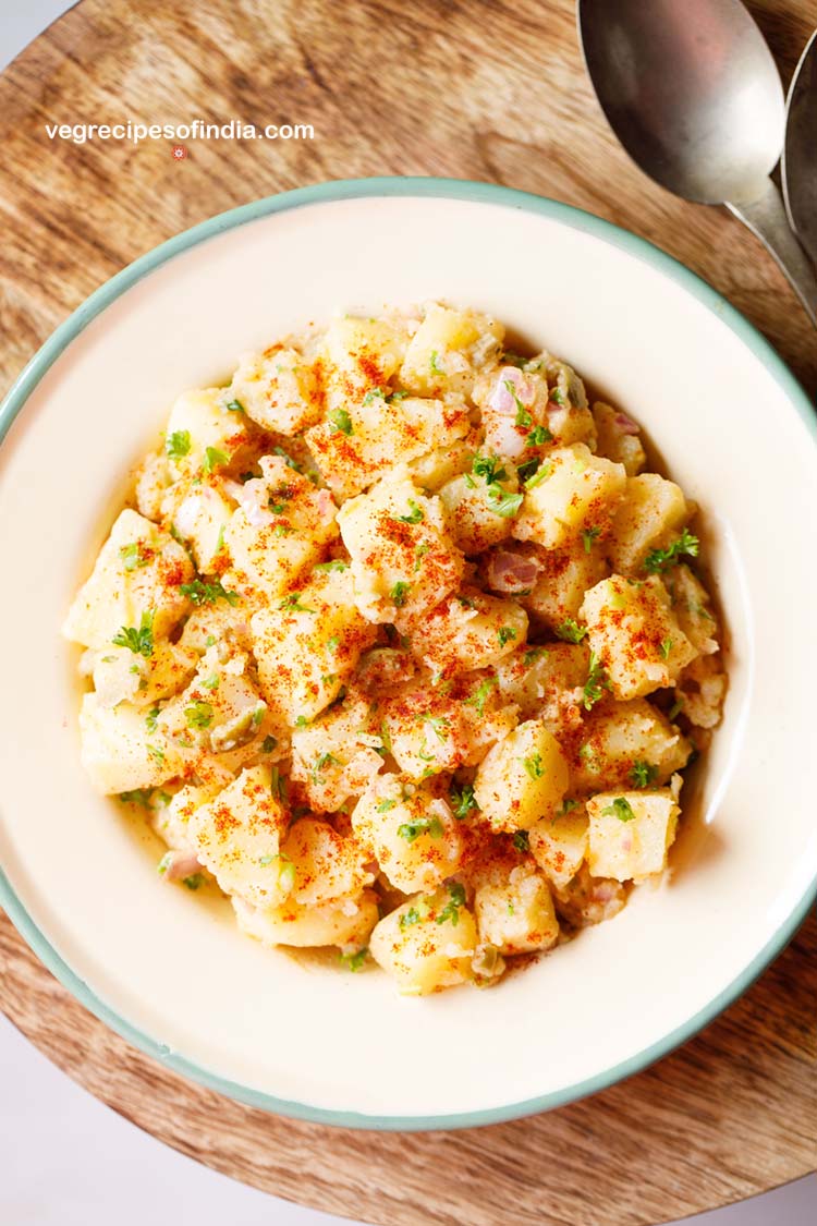 potato salad garnished with parsley, specks of paprika served in a cream enamel plate.