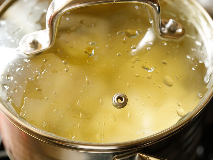 pan covered with glass lid and potatoes being boiled.