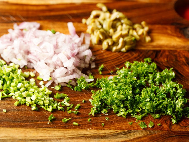 minced onions, celery, olives, parsley on a wooden board.