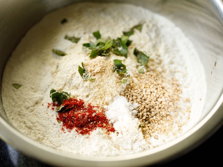 chopped curry leaves, asafoetida, red chili powder, white sesame seeds and salt added to the flours. 