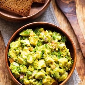 avocado salad served in a wooden bowl with a wooden spoon and some toasted bread in the background