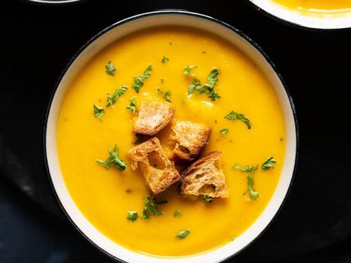 carrot soup in a cream bowl with croutons and chopped parsley on top